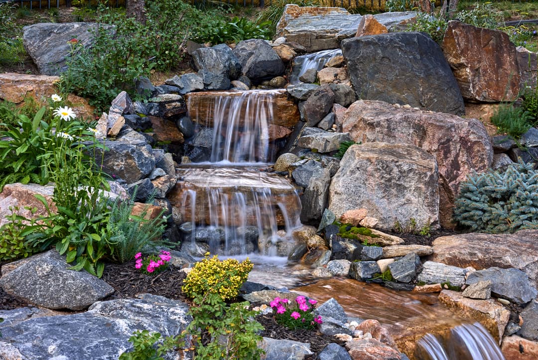 tranquil stone waterfall surrounded by vibrant flowers and lush greenery in a garden setting