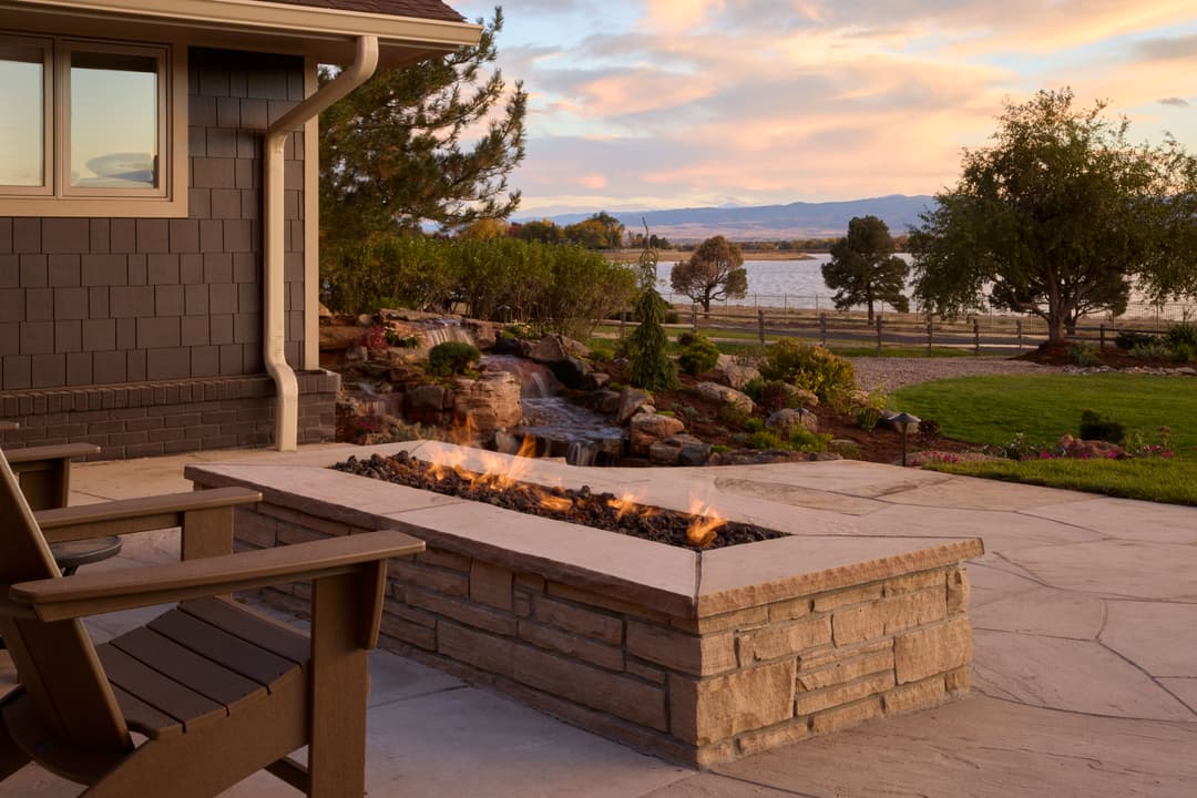 Cozy outdoor patio with fire pit, serene lake view, and sunset over the landscape.