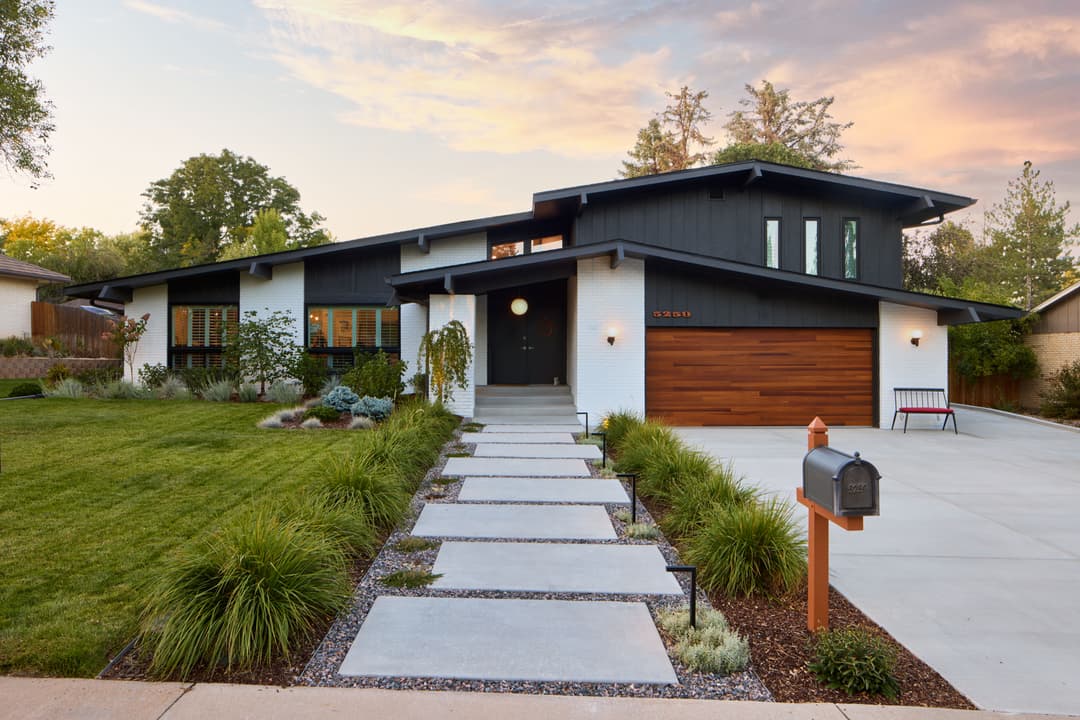 Modern black and white home with wooden accents and landscaped garden at sunset.