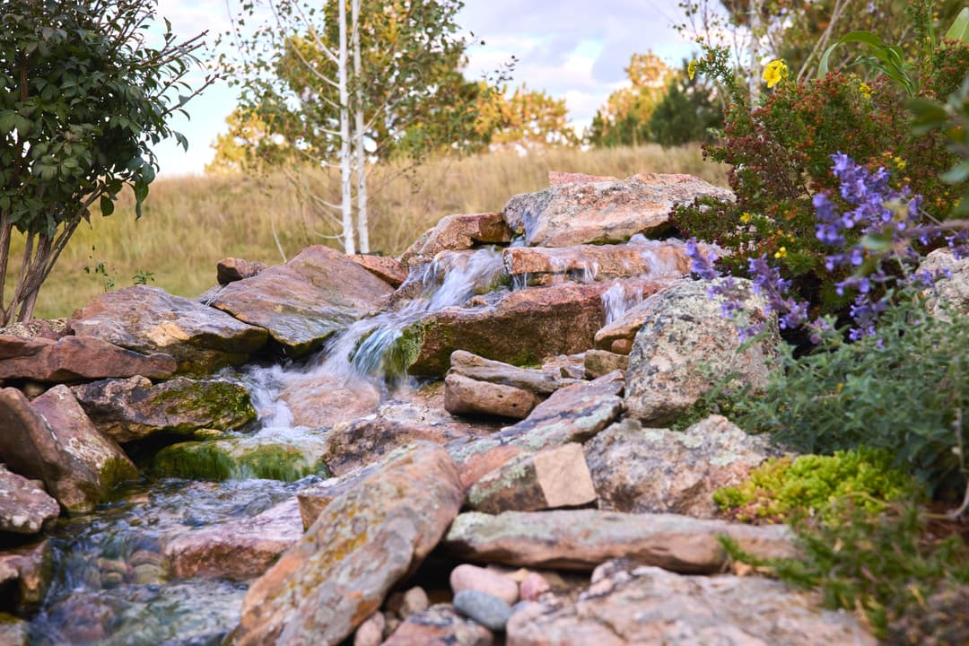 Vibrant garden waterfall cascading over rocks, surrounded by colorful flowers and greenery.