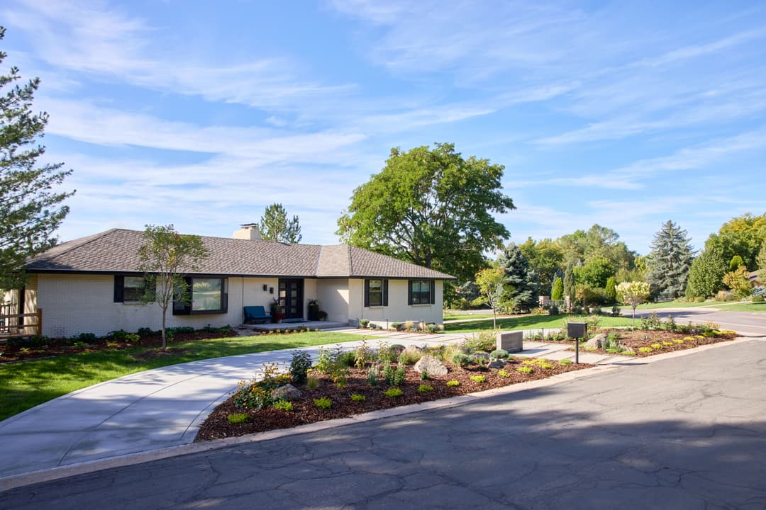 Modern single-story house with lush landscaping and clear blue sky, located on a quiet street.