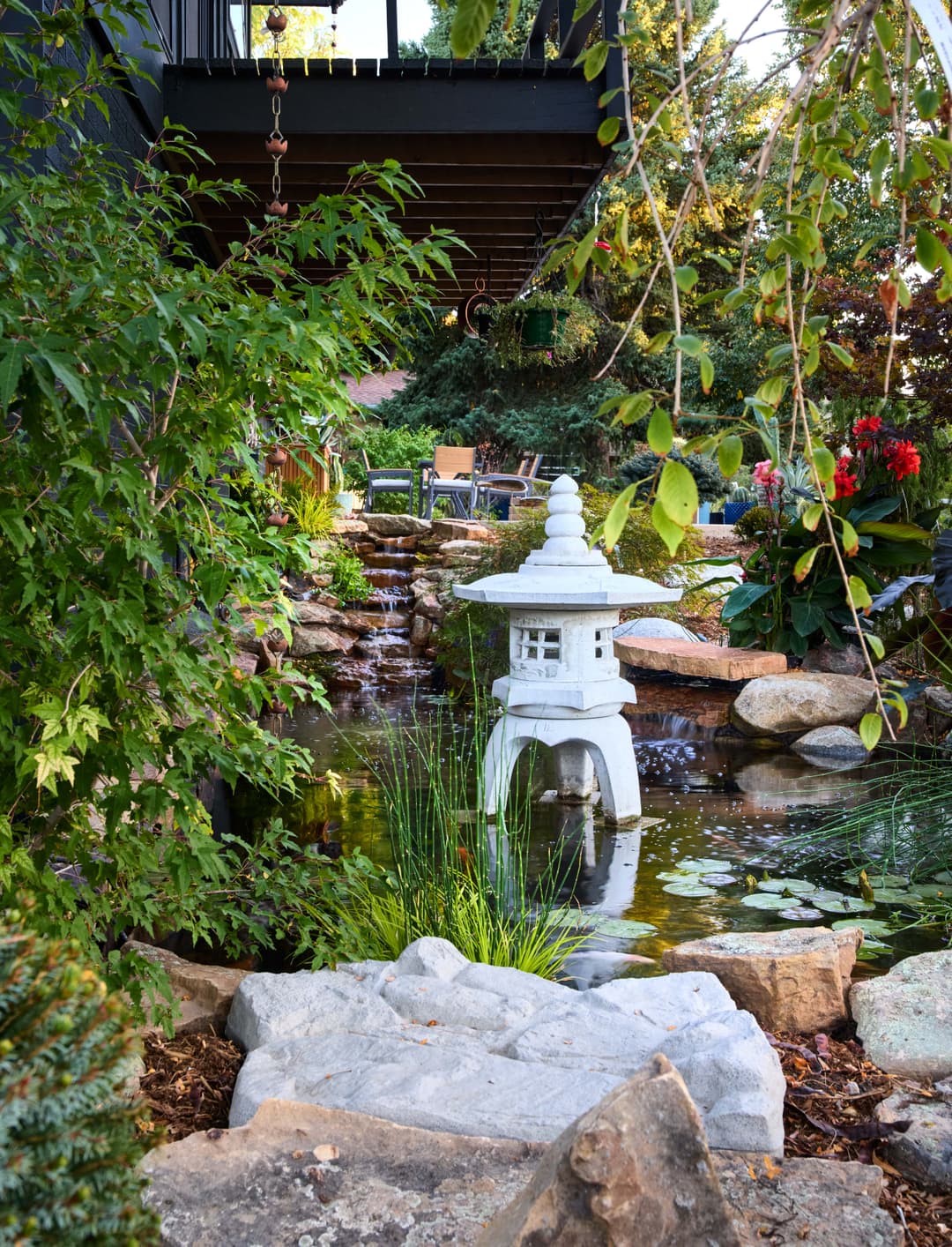Stone lantern by a tranquil pond with lush greenery and rocks in a serene garden setting.