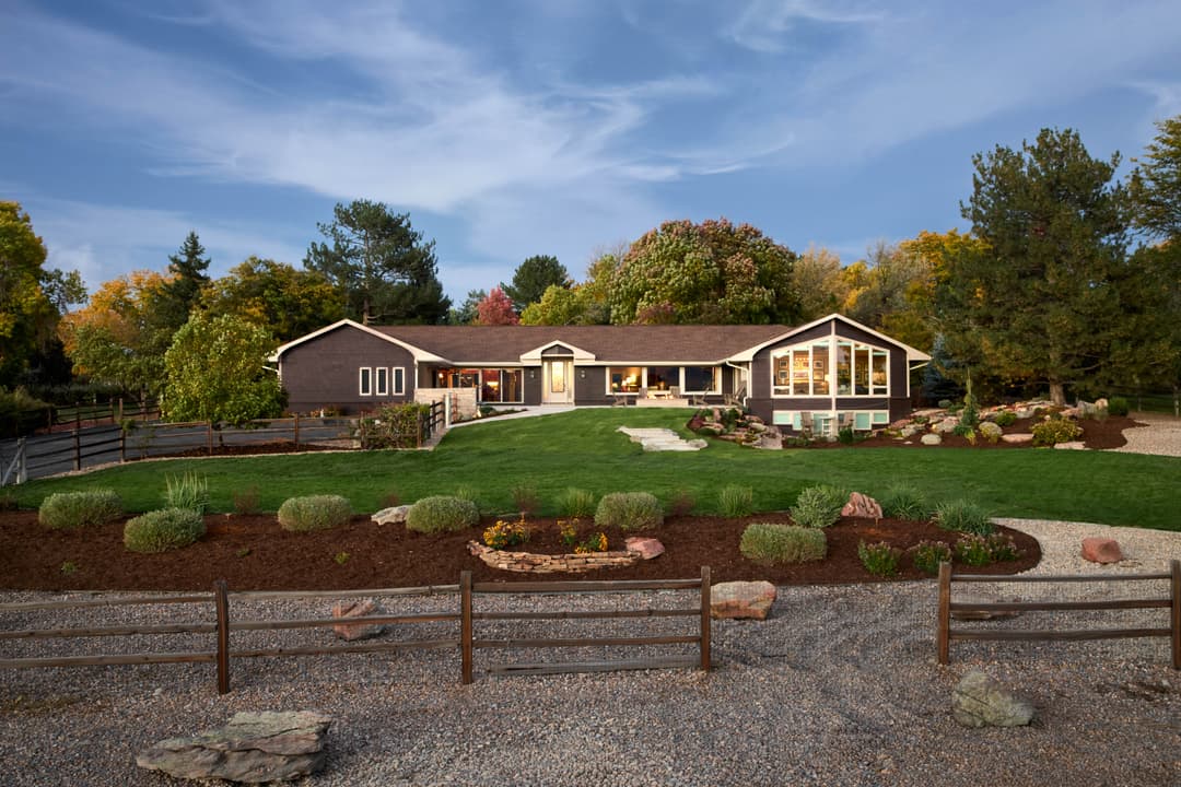 Scenic modern ranch-style home with landscaped yard and stone pathways. Autumn trees in background.