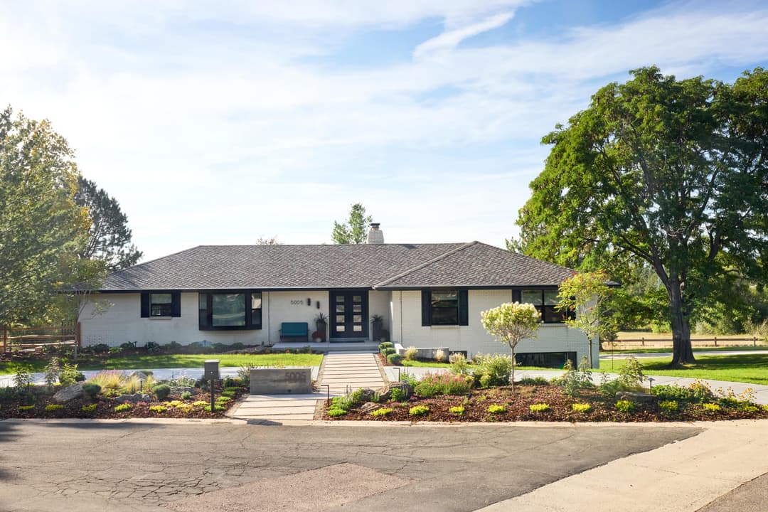 Modern single-story house with landscaped yard and stone pathway, surrounded by trees.