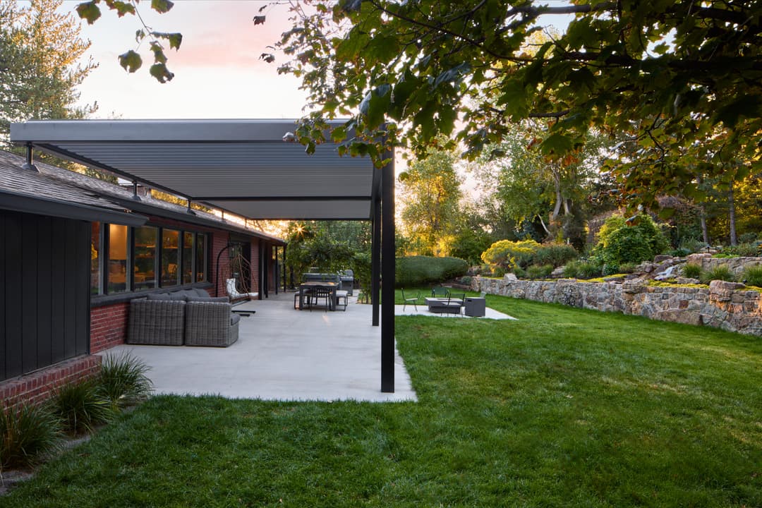 Modern backyard patio with dining area, lush lawn, and stone landscaping at sunset.