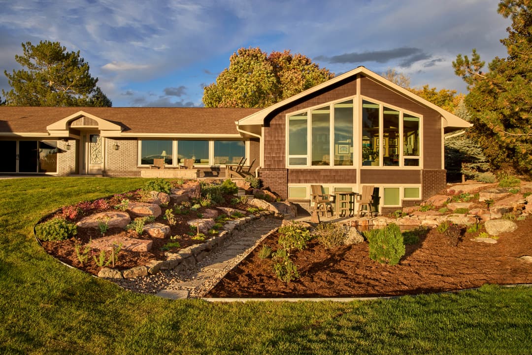 Modern home exterior with landscaped garden, large windows, and outdoor seating area.