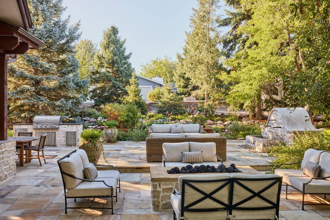 Beautiful outdoor patio with seating, fire pit, grill, and lush greenery in a serene setting.