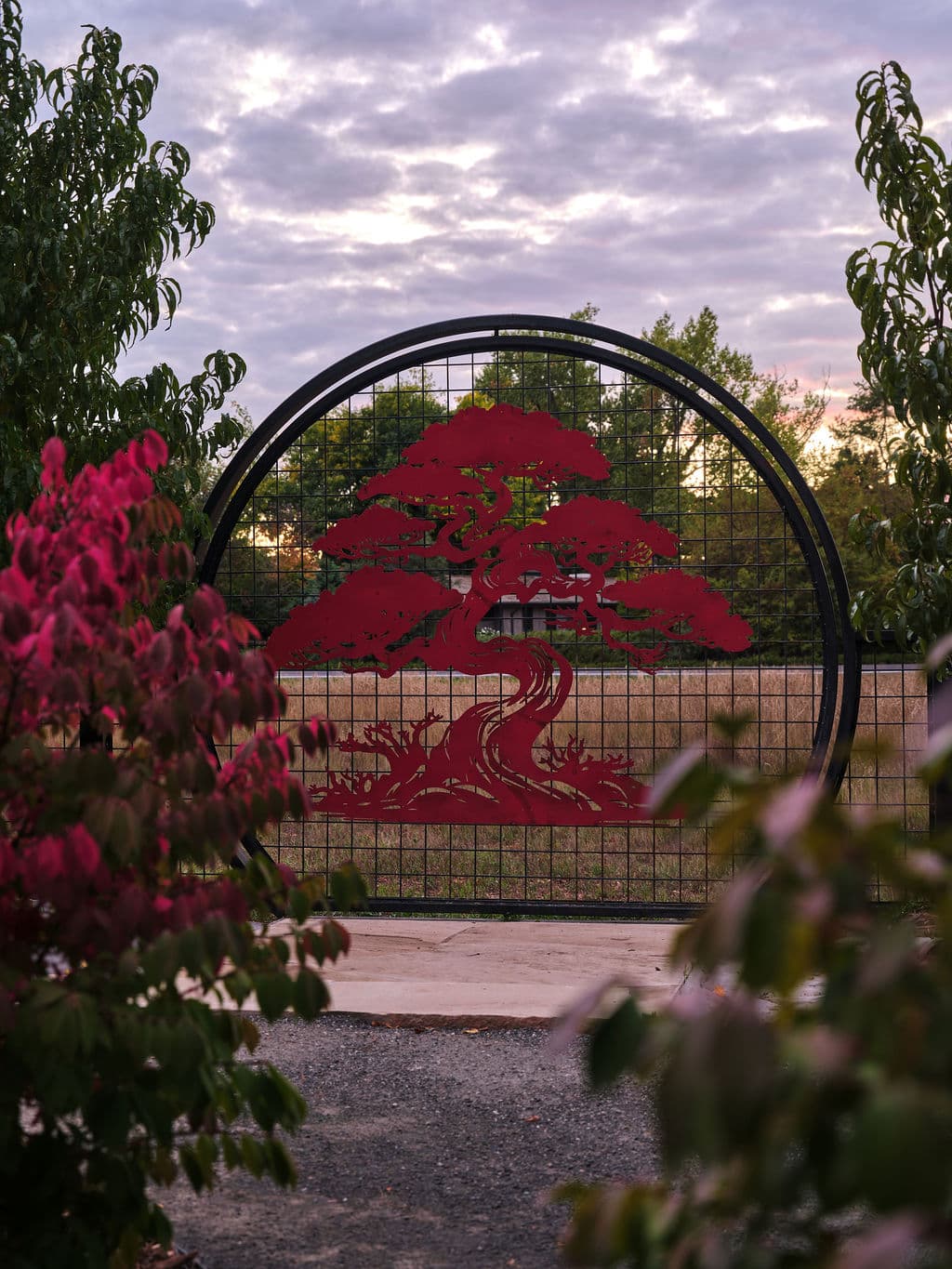 Red tree sculpture gate framed by colorful foliage at sunset. Tranquil outdoor setting.