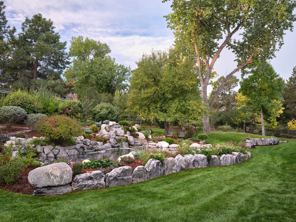 Serene garden landscape with a stone water feature, greenery, and blooming flowers.