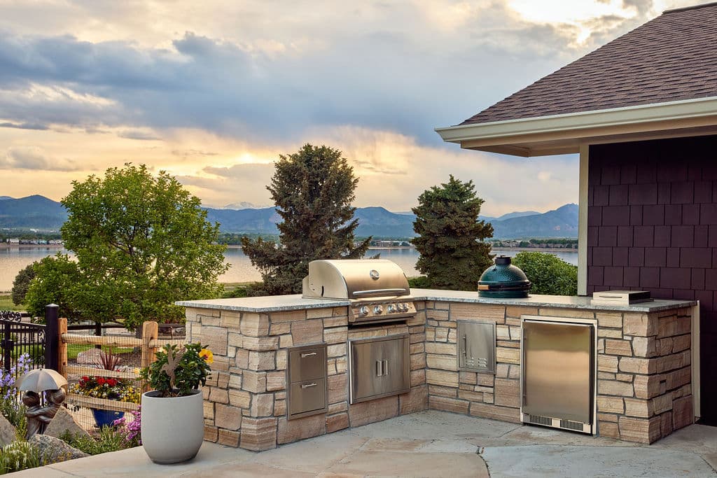 Outdoor kitchen with stainless steel grill, stone counter, and scenic mountain view at sunset.