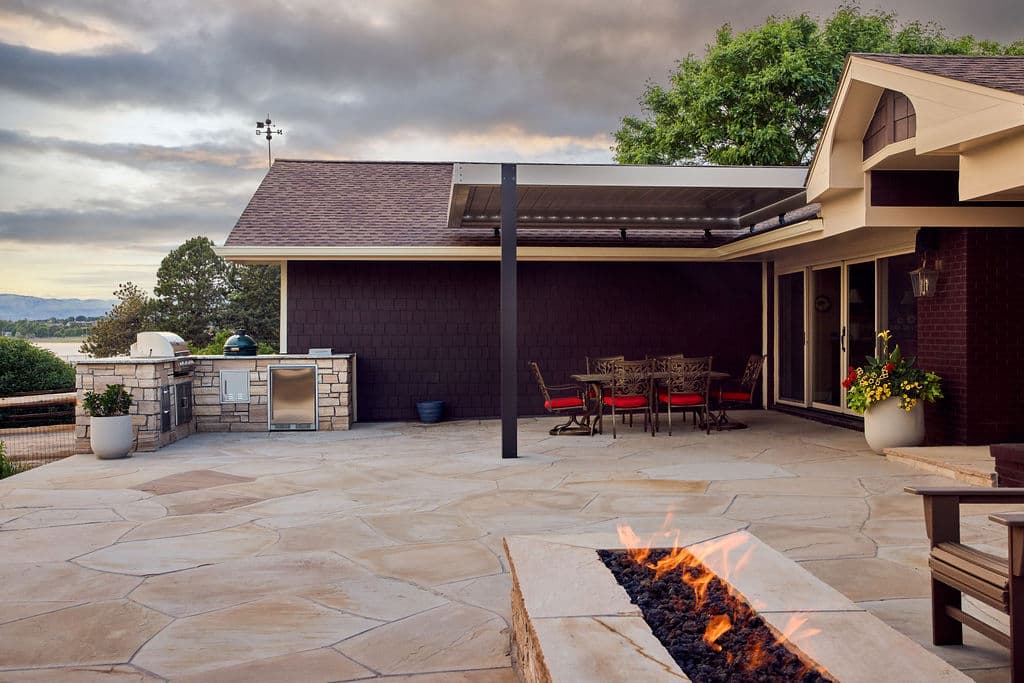 Modern outdoor patio with dining area, grill station, and fire pit against a scenic backdrop.