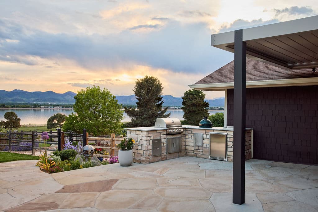 Modern outdoor kitchen with grill, lake view, and mountains at sunset. Perfect for entertaining.