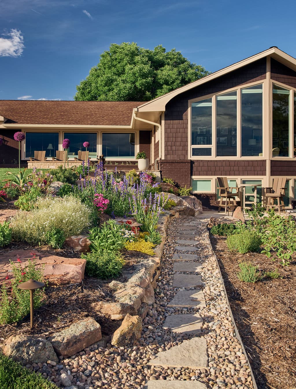 Colorful garden landscape with stone path leading to a modern home under a blue sky.