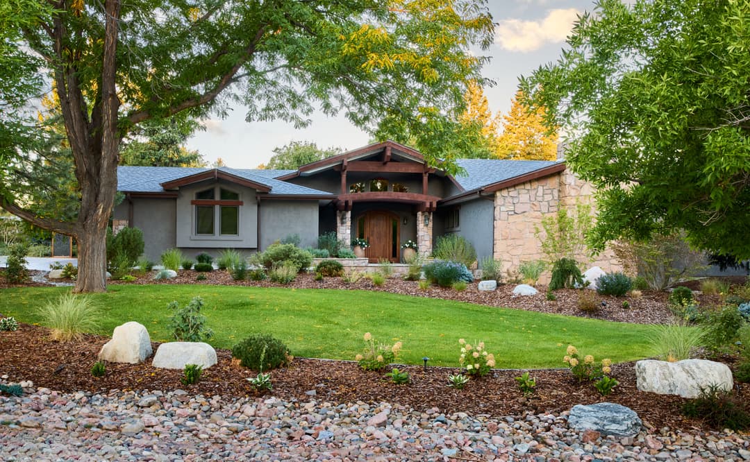 Modern home with stone accents and landscaped garden, featuring lush greenery and decorative rocks.