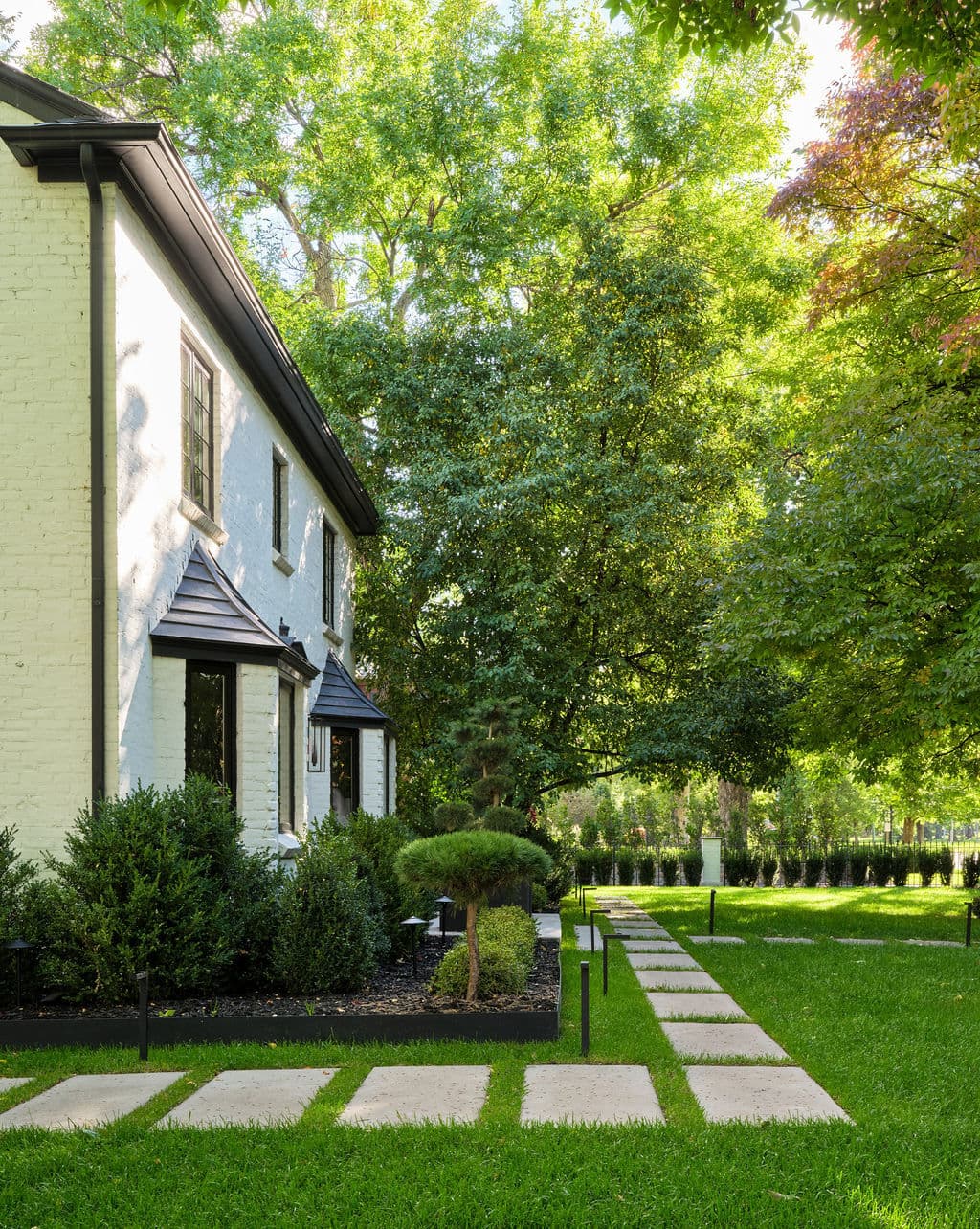 Modern home exterior with lush green landscaping and stone pathway under sunlight.