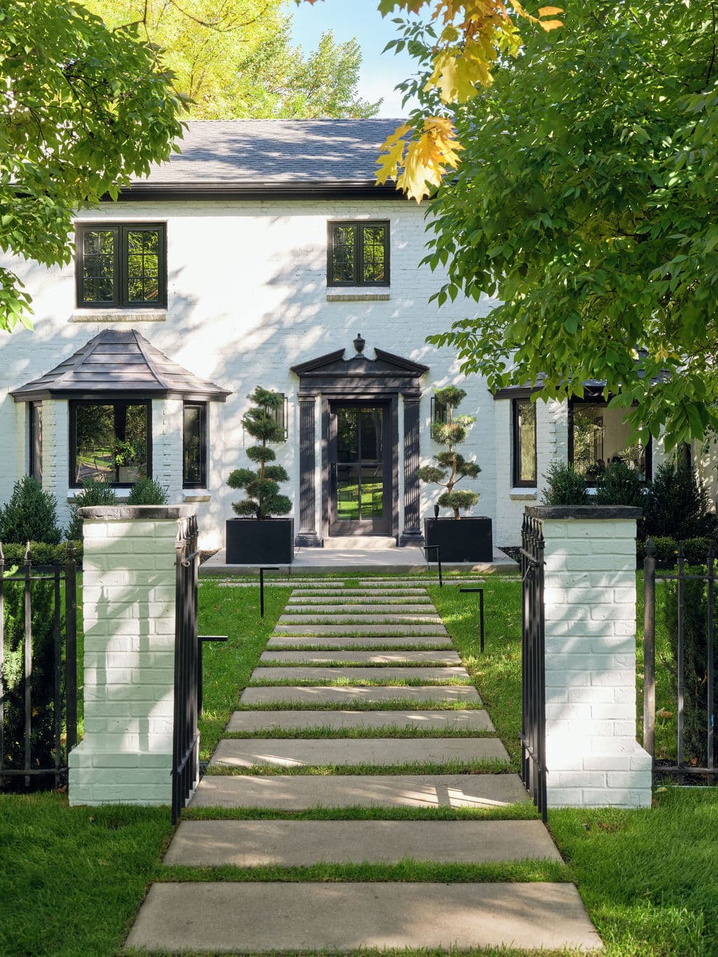 Modern white brick house with black door, landscaped yard, and stone pathway.