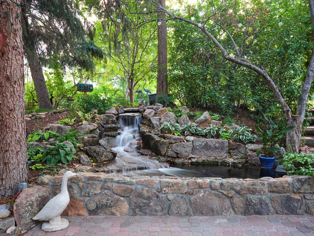 Serene garden with a stone waterfall, lush greenery, and a decorative goose statue.