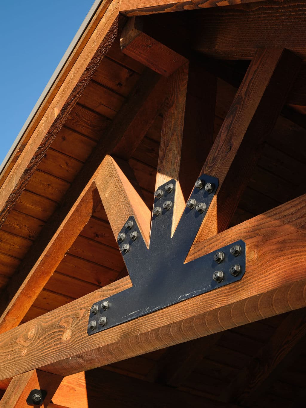 Black metal bracket on wooden roof beams, enhancing architectural detail against blue sky.