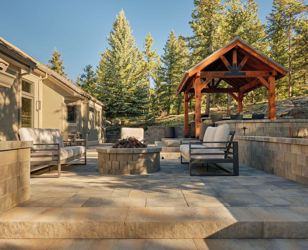 Cozy outdoor seating area with a fire pit and gazebo, surrounded by tall trees.