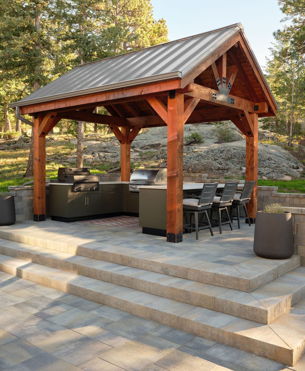Outdoor kitchen pavilion with grilling station and dining area surrounded by trees.