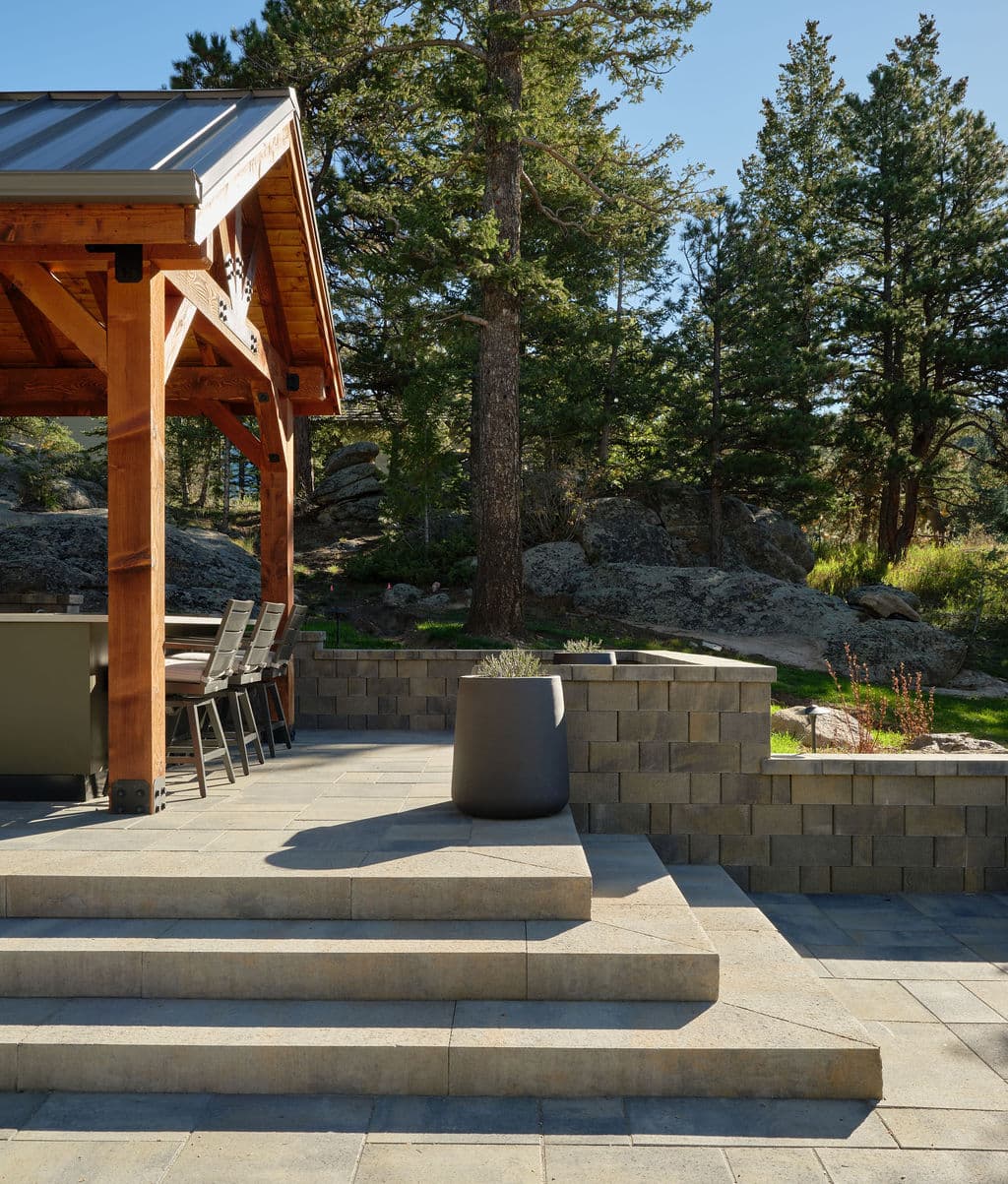 Outdoor patio featuring steps, a gazebo, and stylish planter amidst lush trees and rocks.