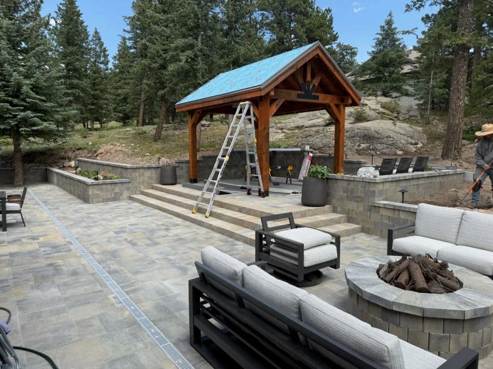 Modern outdoor patio with a gazebo, seating area, and landscaping in a forested setting.